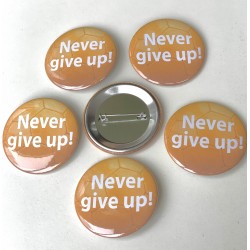 Button Never Give Up met witte tekst op oranje voetbal