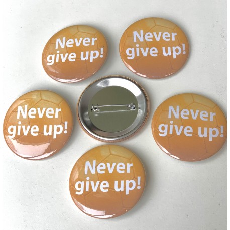 Button Never Give Up met witte tekst op oranje voetbal